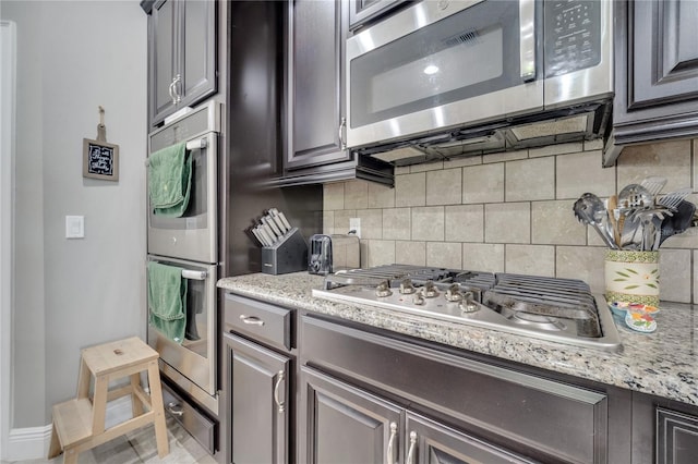 kitchen with tile patterned flooring, tasteful backsplash, light stone counters, and stainless steel appliances