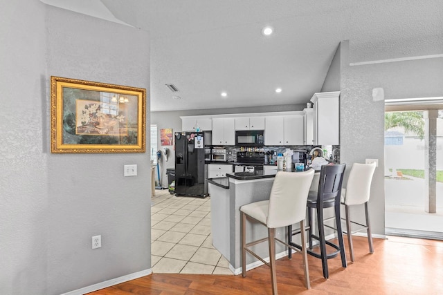 kitchen featuring black appliances, white cabinetry, kitchen peninsula, light tile patterned flooring, and a breakfast bar area