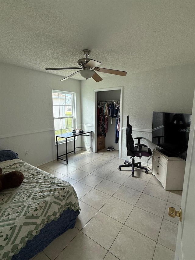 bedroom with ceiling fan, a closet, light tile patterned flooring, and a textured ceiling