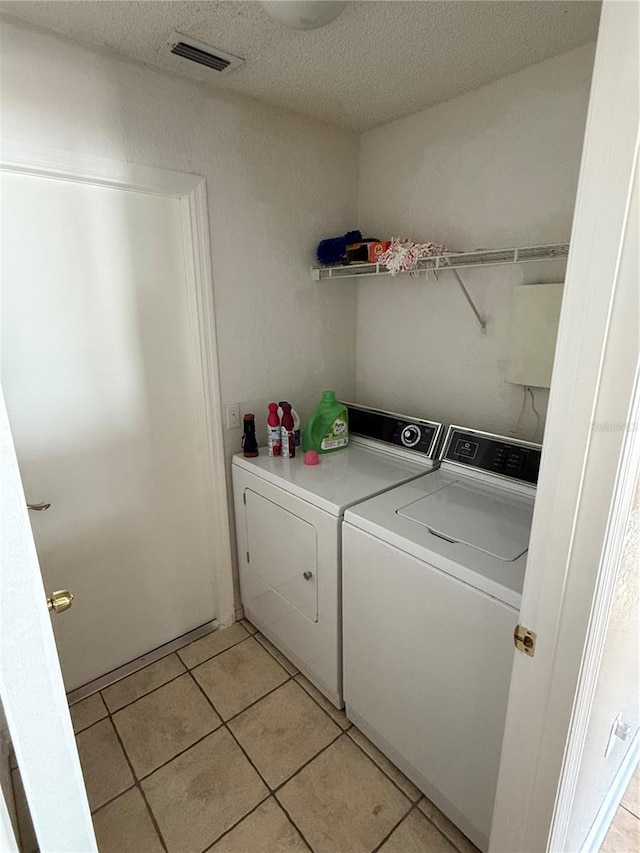 clothes washing area with a textured ceiling, light tile patterned flooring, and washing machine and clothes dryer