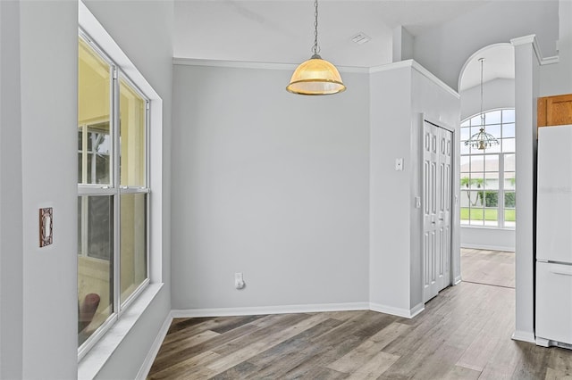 unfurnished dining area with vaulted ceiling, an inviting chandelier, and wood-type flooring