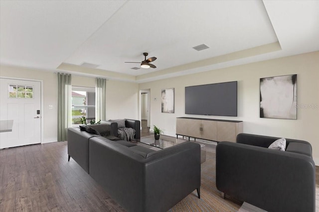 living room featuring ceiling fan, a raised ceiling, and dark hardwood / wood-style floors