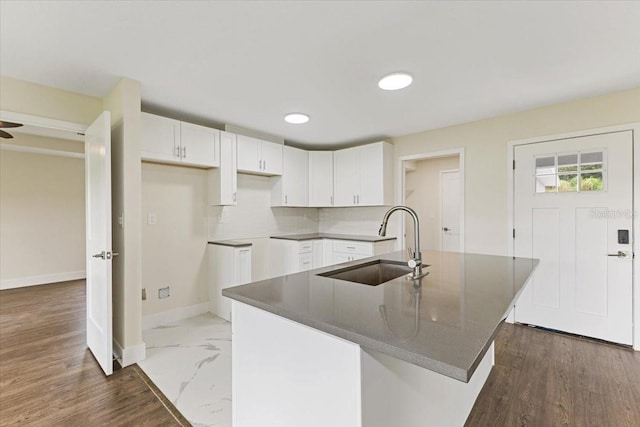 kitchen featuring decorative backsplash, white cabinets, an island with sink, and hardwood / wood-style flooring