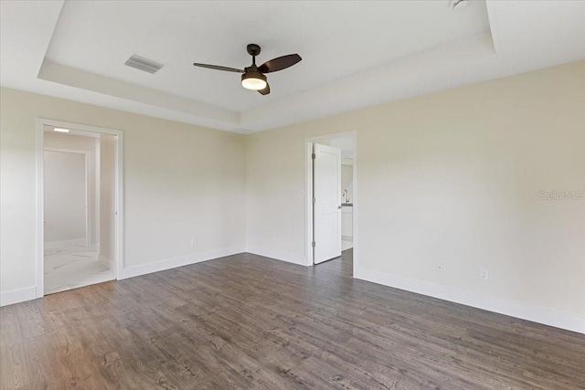 empty room featuring dark wood-type flooring, ceiling fan, and a raised ceiling