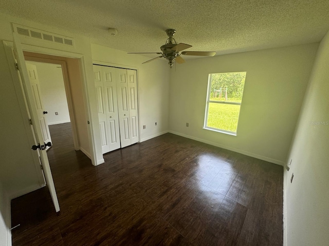 unfurnished bedroom featuring a textured ceiling, dark hardwood / wood-style flooring, a closet, and ceiling fan