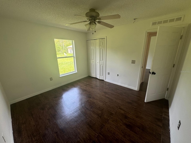 unfurnished bedroom with dark wood-type flooring, a textured ceiling, ceiling fan, and a closet