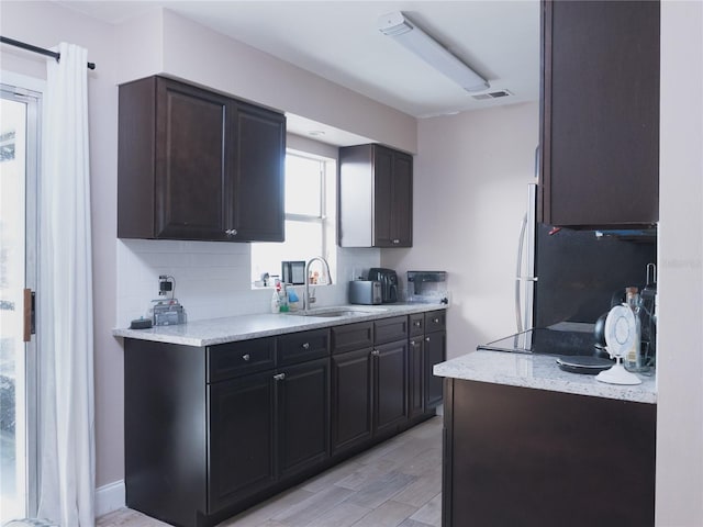 kitchen featuring tasteful backsplash, dark brown cabinetry, stainless steel fridge, and sink