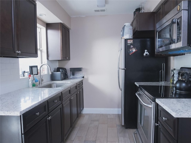 kitchen featuring sink, tasteful backsplash, light stone counters, dark brown cabinets, and appliances with stainless steel finishes