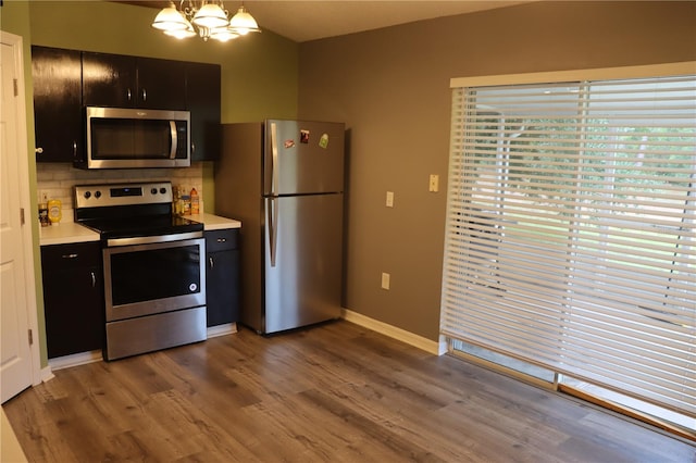 kitchen featuring tasteful backsplash, a chandelier, hardwood / wood-style floors, appliances with stainless steel finishes, and pendant lighting