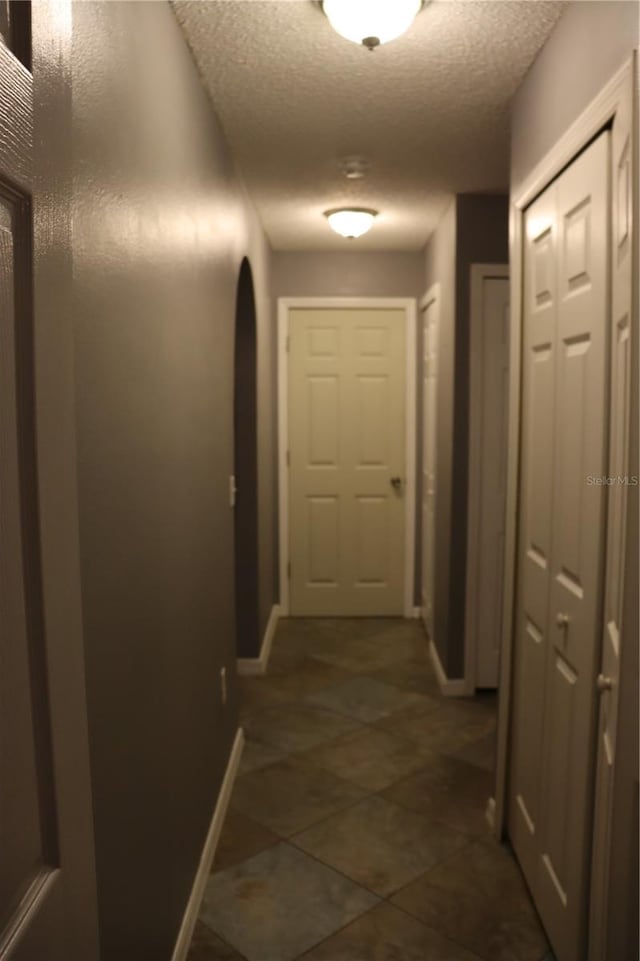 hallway featuring dark tile patterned flooring and a textured ceiling