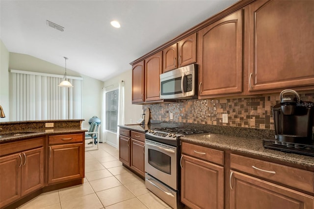 kitchen with decorative light fixtures, vaulted ceiling, dark stone countertops, light tile patterned floors, and stainless steel appliances