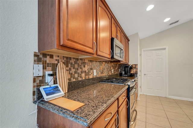 kitchen with lofted ceiling, light tile patterned floors, dark stone countertops, backsplash, and stainless steel appliances