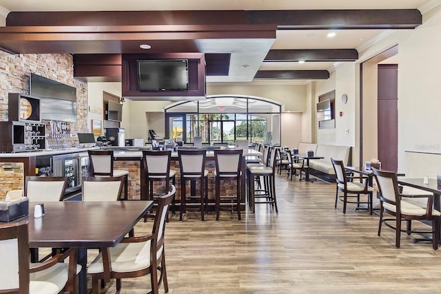 dining area with bar area, beam ceiling, and light hardwood / wood-style floors