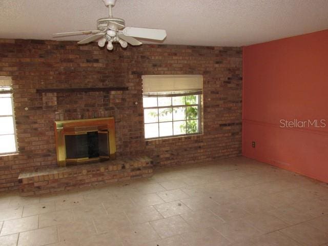 unfurnished living room featuring a fireplace, a wealth of natural light, a textured ceiling, and ceiling fan