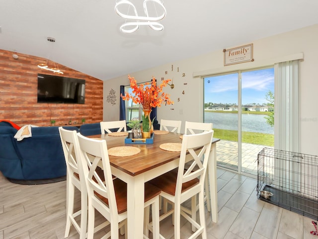 dining room featuring lofted ceiling, a water view, wood walls, and light hardwood / wood-style flooring