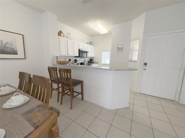 kitchen with appliances with stainless steel finishes, light tile patterned floors, white cabinets, and kitchen peninsula