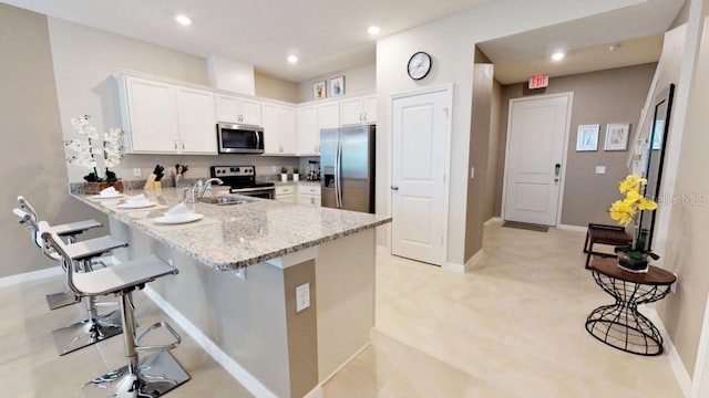 kitchen with light tile patterned floors, kitchen peninsula, white cabinets, stainless steel appliances, and light stone countertops