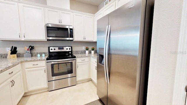 kitchen with appliances with stainless steel finishes, light stone counters, white cabinets, and light tile patterned floors