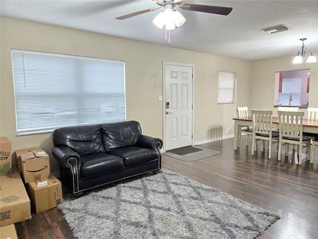 living room featuring dark wood-type flooring, a textured ceiling, and ceiling fan with notable chandelier