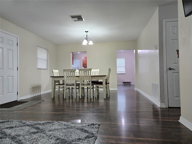 dining area featuring dark wood-type flooring, a textured ceiling, and a chandelier