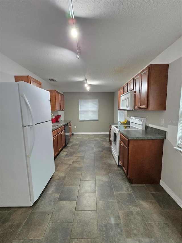 kitchen with a textured ceiling, white appliances, dark tile patterned flooring, and track lighting