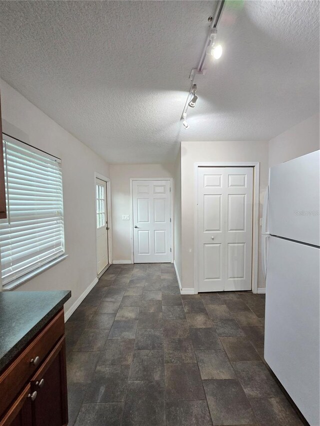 interior space featuring dark tile patterned flooring, track lighting, a textured ceiling, and white fridge