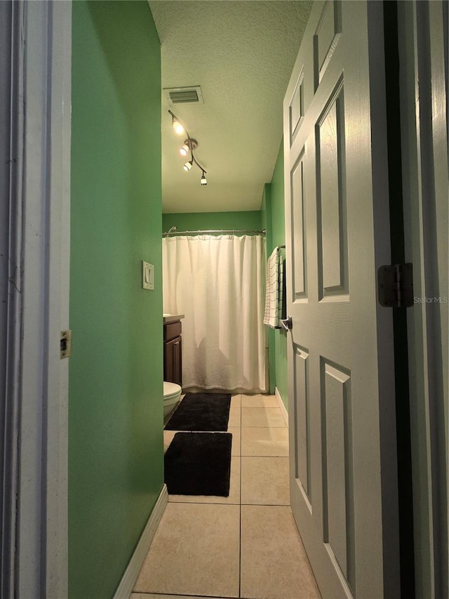 bathroom with a textured ceiling, toilet, vanity, tile patterned flooring, and track lighting