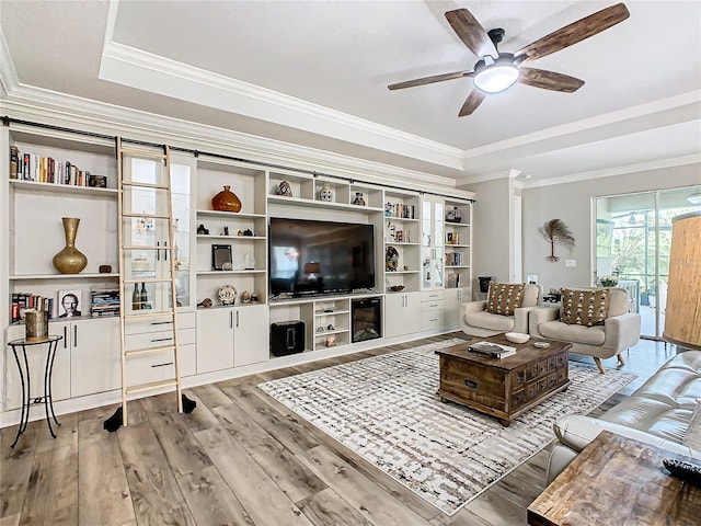 living room with wood-type flooring, ornamental molding, ceiling fan, and a raised ceiling