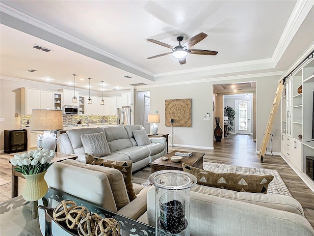 living room featuring ceiling fan, crown molding, a tray ceiling, and dark hardwood / wood-style flooring