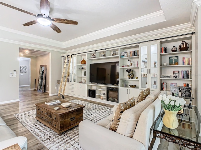 living room featuring crown molding, a fireplace, light hardwood / wood-style flooring, ceiling fan, and a tray ceiling