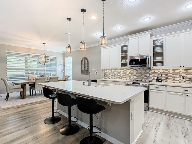 kitchen featuring appliances with stainless steel finishes, a kitchen island with sink, sink, white cabinets, and a breakfast bar