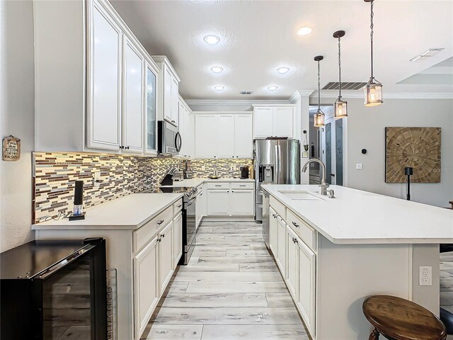 kitchen featuring white cabinets, pendant lighting, stainless steel appliances, a center island with sink, and beverage cooler