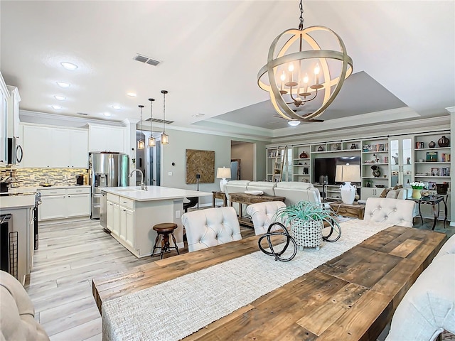 dining room with light hardwood / wood-style floors, crown molding, a raised ceiling, and an inviting chandelier