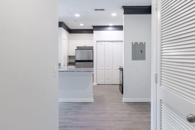 kitchen with stainless steel refrigerator, white cabinetry, electric panel, crown molding, and light wood-type flooring