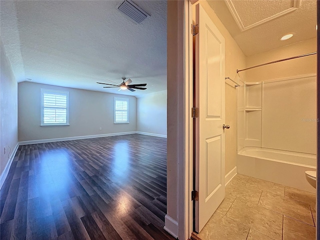 interior space with ceiling fan,  shower combination, toilet, and a textured ceiling