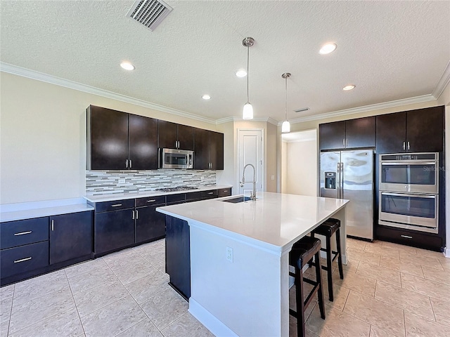 kitchen with decorative light fixtures, a center island with sink, sink, dark brown cabinetry, and appliances with stainless steel finishes