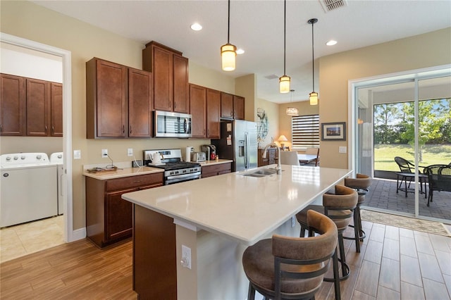 kitchen featuring independent washer and dryer, stainless steel appliances, a kitchen breakfast bar, and a kitchen island with sink