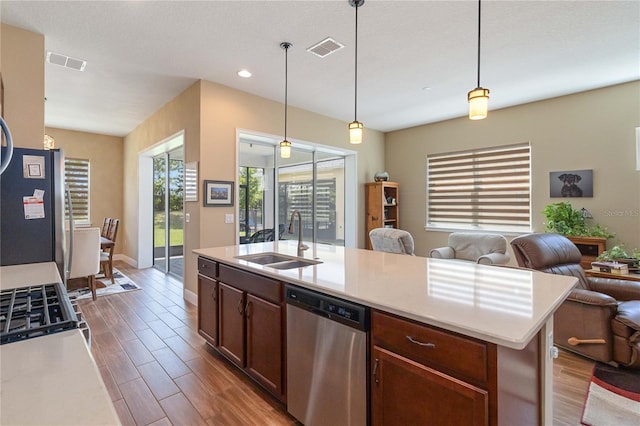 kitchen featuring hanging light fixtures, appliances with stainless steel finishes, sink, and a center island with sink