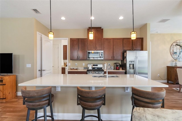 kitchen featuring stainless steel appliances, an island with sink, pendant lighting, and a kitchen bar