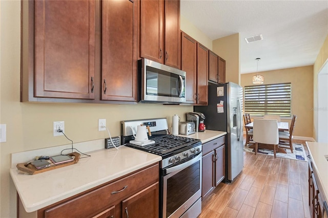 kitchen featuring stainless steel appliances, hanging light fixtures, and light wood-type flooring