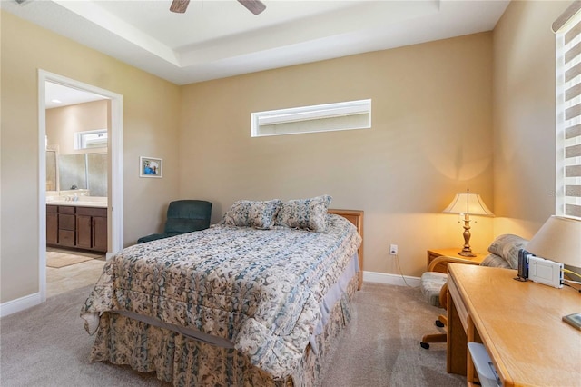 bedroom featuring ensuite bathroom, light colored carpet, ceiling fan, and a tray ceiling