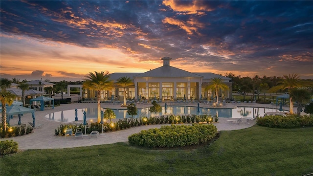 pool at dusk featuring a patio and a lawn