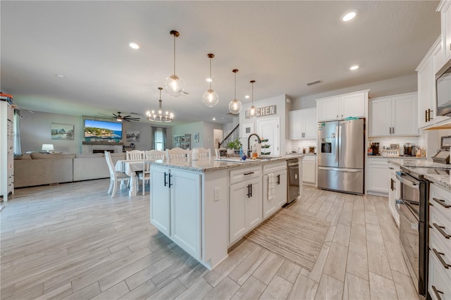 kitchen featuring appliances with stainless steel finishes, pendant lighting, white cabinetry, an island with sink, and light stone countertops