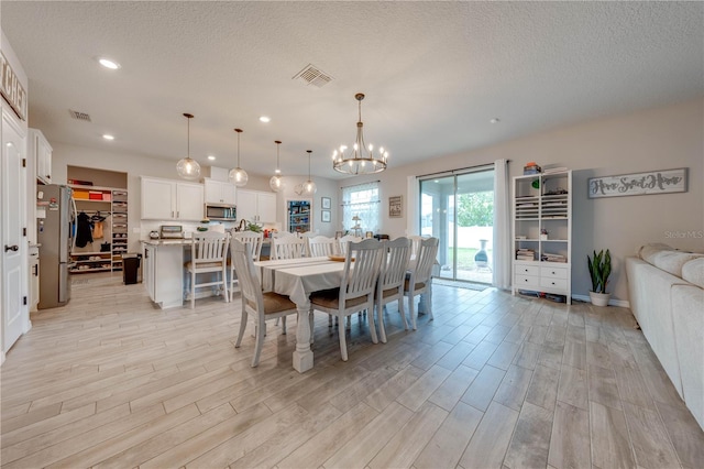 dining space featuring an inviting chandelier, a textured ceiling, and light hardwood / wood-style flooring