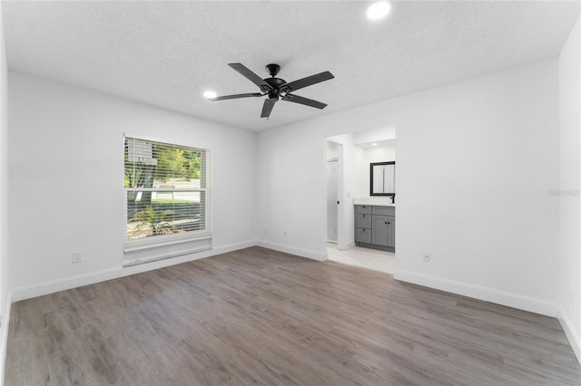 unfurnished room with a ceiling fan, light wood-style flooring, baseboards, and a textured ceiling