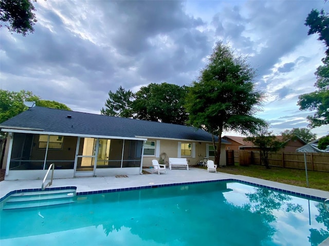 rear view of property featuring a sunroom, a patio area, fence, and a fenced in pool