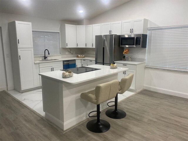 kitchen with light countertops, appliances with stainless steel finishes, white cabinets, a sink, and a kitchen bar