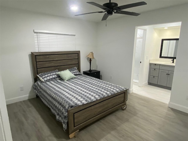 bedroom featuring baseboards, ensuite bath, a sink, and light wood-style floors