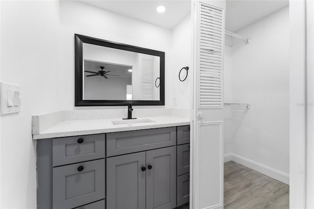 bathroom with recessed lighting, wood finished floors, vanity, baseboards, and a spacious closet