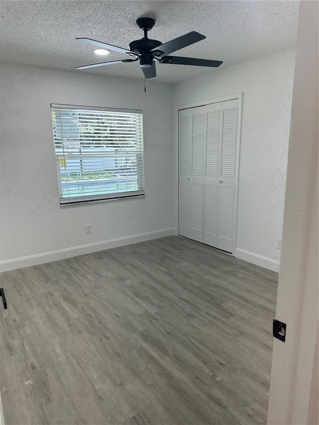 unfurnished bedroom featuring a textured ceiling, a closet, wood finished floors, and baseboards